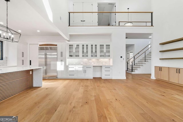 unfurnished living room with stairs, an inviting chandelier, light wood-style flooring, and a towering ceiling