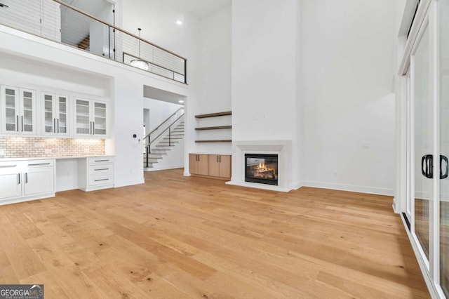 unfurnished living room featuring a glass covered fireplace, baseboards, light wood-style flooring, and stairs