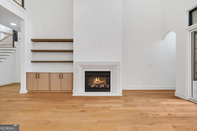 unfurnished living room featuring baseboards, a glass covered fireplace, and light wood finished floors