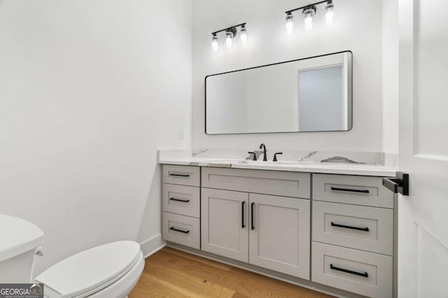 half bath featuring toilet, vanity, baseboards, and wood finished floors