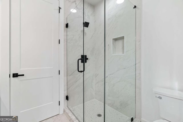 bathroom featuring a marble finish shower and toilet