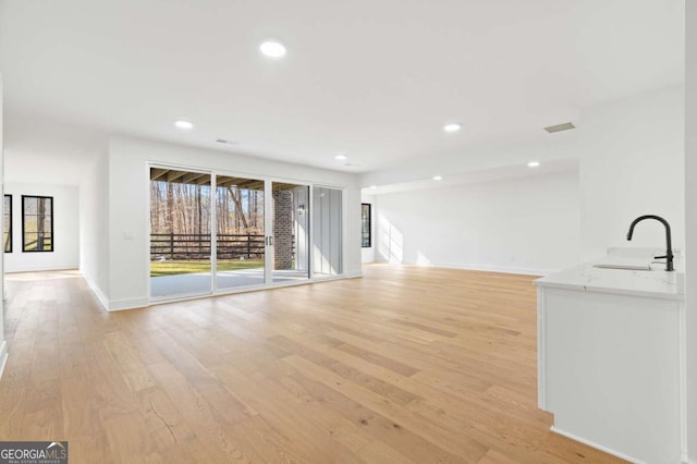 unfurnished living room with visible vents, baseboards, recessed lighting, light wood-style flooring, and a sink