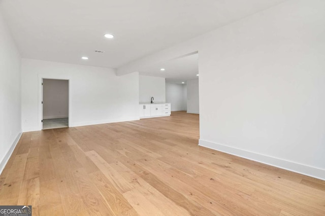 unfurnished living room with recessed lighting, light wood-style floors, baseboards, and a sink