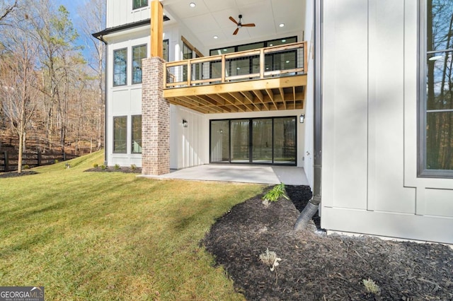 rear view of house featuring a patio, a balcony, a ceiling fan, a lawn, and board and batten siding