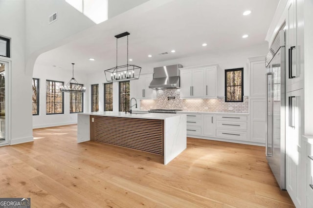 kitchen featuring visible vents, arched walkways, a sink, wall chimney exhaust hood, and light wood-type flooring