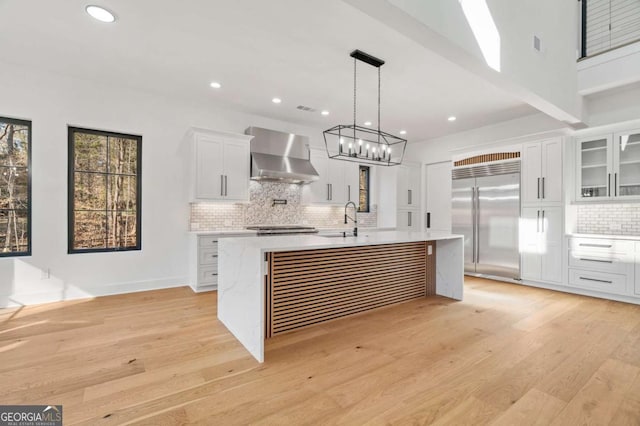 kitchen featuring a sink, wall chimney range hood, built in fridge, light wood-style floors, and light countertops