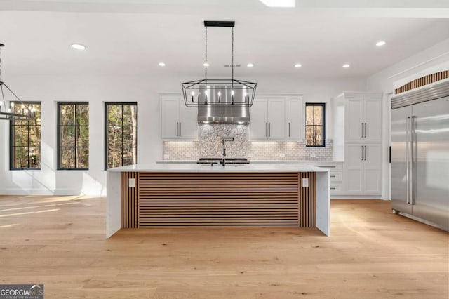 kitchen with light wood finished floors, a kitchen island with sink, a sink, stainless steel built in fridge, and light countertops