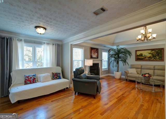 living room featuring a textured ceiling, a notable chandelier, light wood-type flooring, a tray ceiling, and crown molding