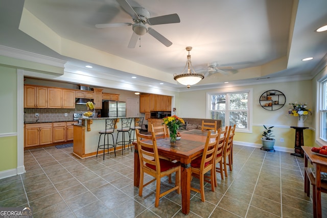 tiled dining space featuring ceiling fan, ornamental molding, and a raised ceiling