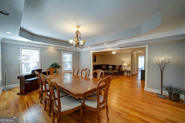 dining area featuring crown molding, light wood-type flooring, an inviting chandelier, and a raised ceiling