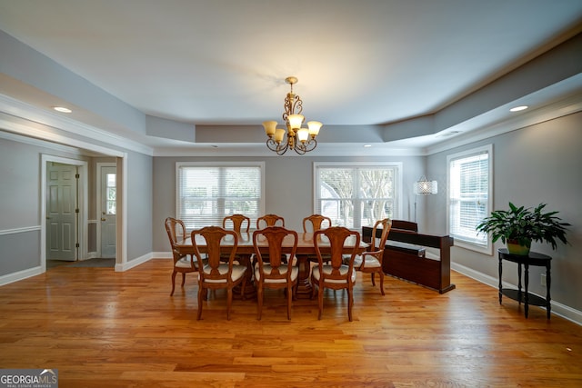 dining room featuring a raised ceiling, a chandelier, light hardwood / wood-style floors, and crown molding