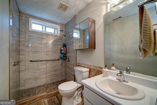 bathroom featuring toilet, a tile shower, vanity, and a textured ceiling