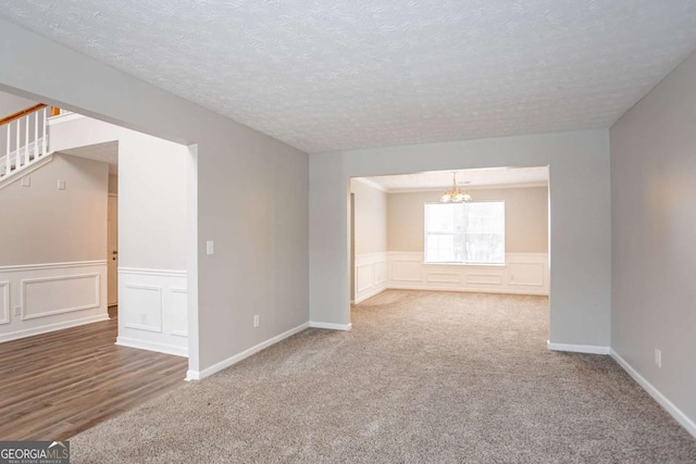 empty room with carpet floors, a textured ceiling, and a notable chandelier