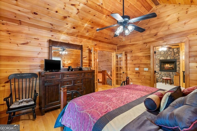 bedroom with wood ceiling, a stone fireplace, ceiling fan, light wood-type flooring, and lofted ceiling with beams