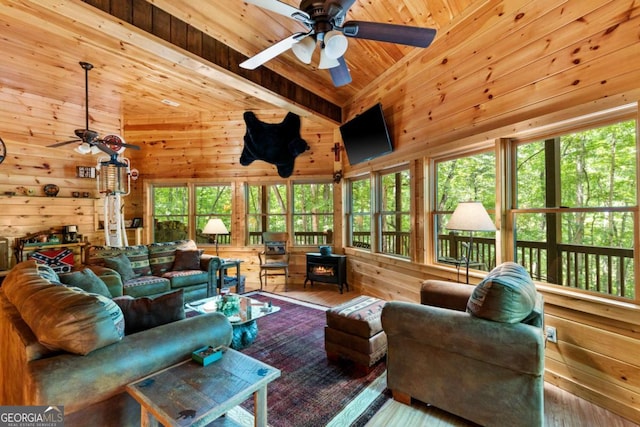 sunroom / solarium with ceiling fan, wooden ceiling, a wood stove, and lofted ceiling