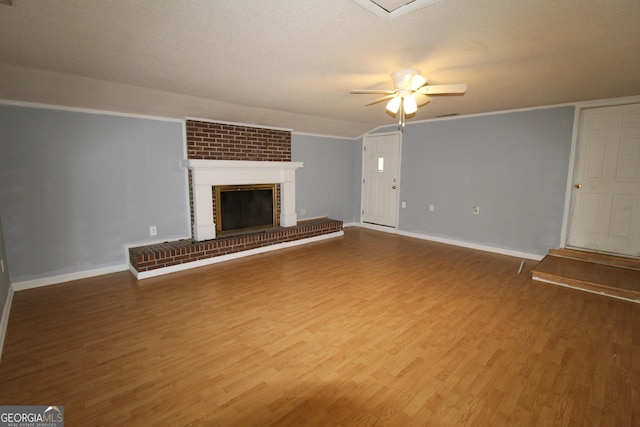 unfurnished living room with a textured ceiling, vaulted ceiling, hardwood / wood-style floors, ceiling fan, and a brick fireplace