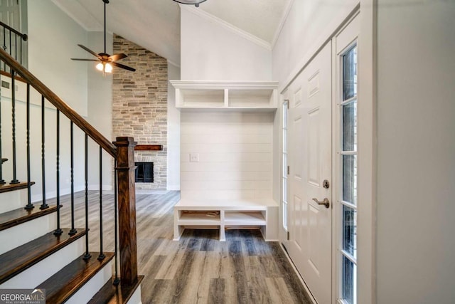 mudroom featuring ceiling fan, wood-type flooring, high vaulted ceiling, crown molding, and a stone fireplace