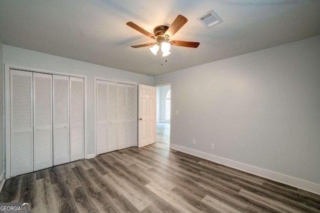 unfurnished bedroom with wood-type flooring, multiple closets, and ceiling fan