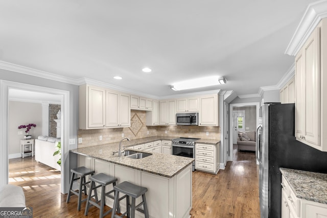 kitchen featuring a kitchen breakfast bar, stainless steel appliances, kitchen peninsula, light stone countertops, and sink