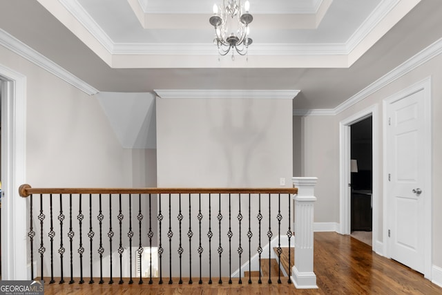 corridor featuring hardwood / wood-style flooring, an inviting chandelier, a tray ceiling, and crown molding