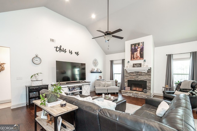 living room with ceiling fan, dark wood-type flooring, a stone fireplace, and a wealth of natural light