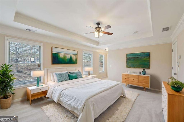 bedroom with a raised ceiling, ceiling fan, multiple windows, and light colored carpet