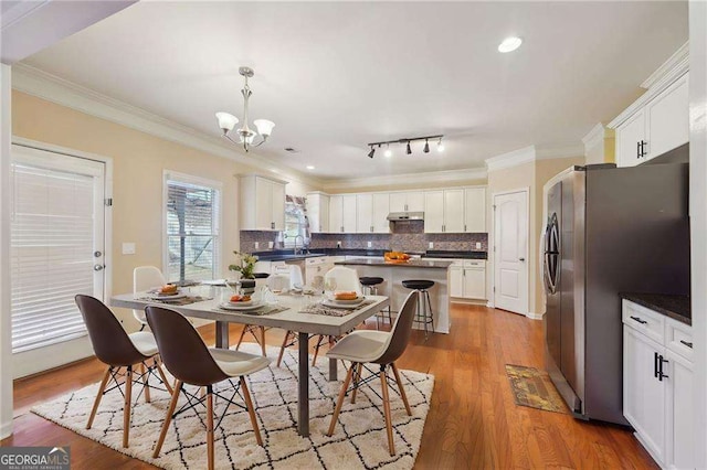 dining space with track lighting, a notable chandelier, crown molding, and light hardwood / wood-style flooring