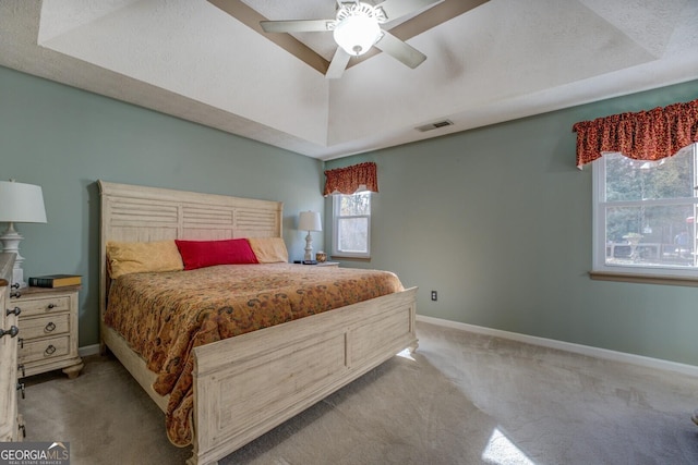 bedroom with a raised ceiling, ceiling fan, and light carpet