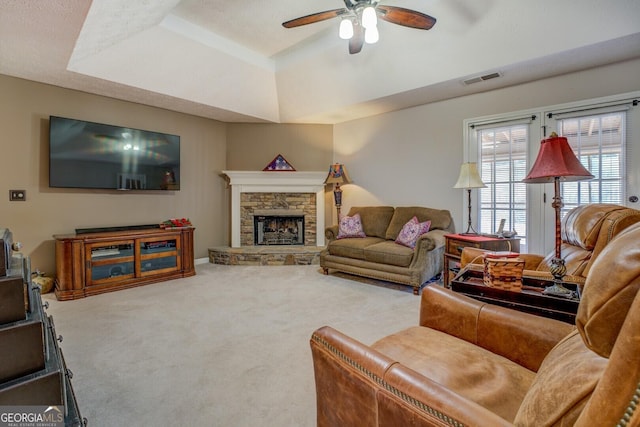 living room with a raised ceiling, ceiling fan, carpet, and a stone fireplace