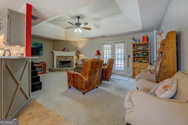 living room with a textured ceiling, a raised ceiling, french doors, light colored carpet, and ceiling fan