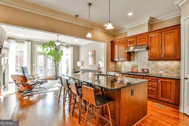 kitchen featuring a kitchen island with sink, hanging light fixtures, stainless steel gas cooktop, sink, and tasteful backsplash