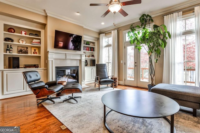 sitting room with ornamental molding, light wood-type flooring, built in features, and ceiling fan