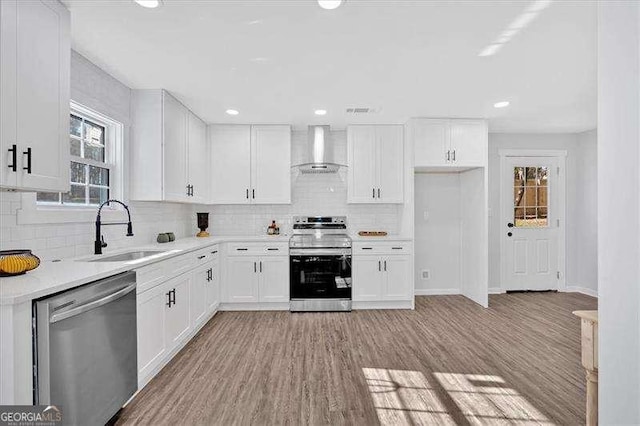 kitchen with white cabinets, stainless steel appliances, light wood-type flooring, wall chimney exhaust hood, and sink