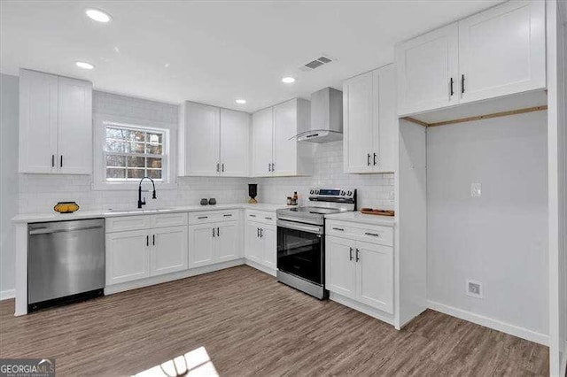 kitchen with wall chimney exhaust hood, light hardwood / wood-style flooring, stainless steel appliances, white cabinetry, and sink