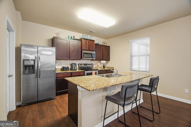 kitchen featuring dark hardwood / wood-style floors, a center island with sink, sink, appliances with stainless steel finishes, and a breakfast bar area