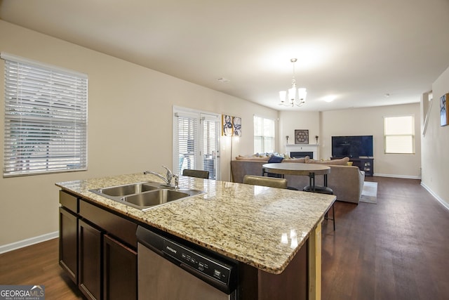 kitchen with pendant lighting, dark brown cabinetry, sink, stainless steel dishwasher, and a center island with sink