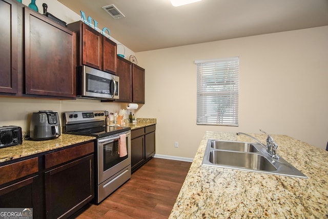 kitchen with light stone countertops, dark brown cabinetry, appliances with stainless steel finishes, sink, and dark hardwood / wood-style floors