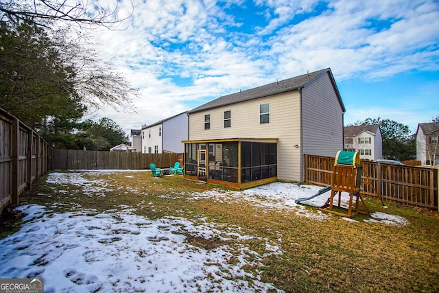 snow covered rear of property featuring a playground and a sunroom