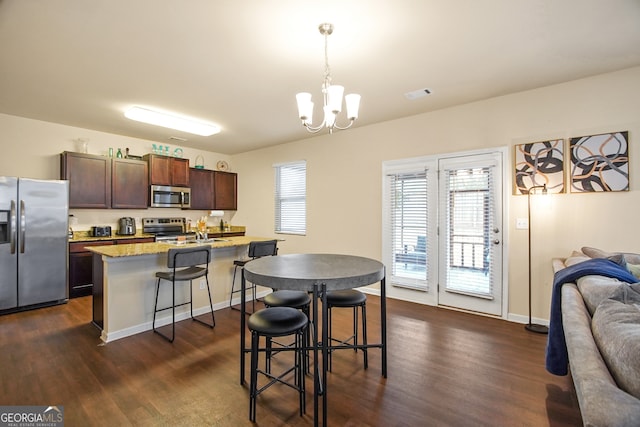 kitchen with decorative light fixtures, a notable chandelier, a center island with sink, a kitchen bar, and appliances with stainless steel finishes