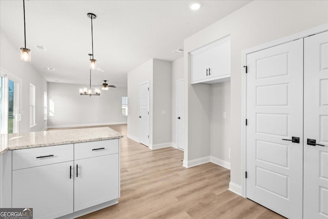 kitchen with hanging light fixtures, white cabinetry, light stone counters, and light hardwood / wood-style flooring