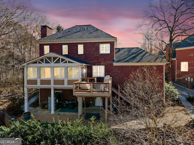 back house at dusk with a deck, a sunroom, and a patio