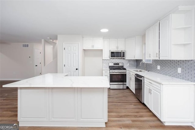 kitchen with sink, stainless steel appliances, light stone countertops, and a kitchen island