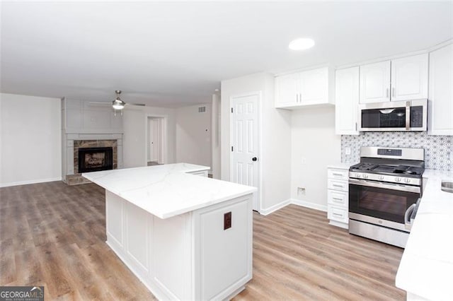 kitchen with stainless steel appliances, ceiling fan, white cabinets, light hardwood / wood-style flooring, and tasteful backsplash