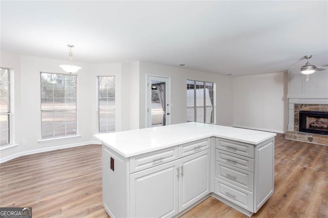 kitchen with a fireplace, white cabinetry, a center island, ceiling fan, and pendant lighting