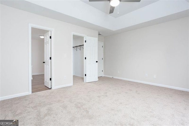 unfurnished bedroom featuring a spacious closet, ensuite bathroom, a closet, light colored carpet, and ceiling fan