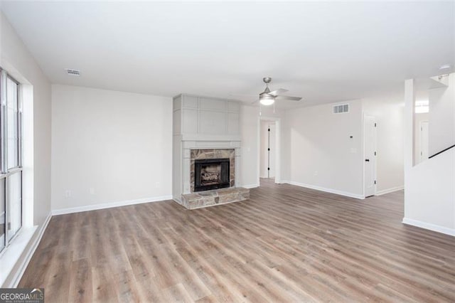 unfurnished living room with light hardwood / wood-style floors, ceiling fan, and a stone fireplace