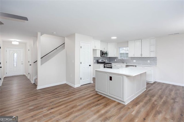 kitchen with a center island, light hardwood / wood-style floors, tasteful backsplash, white cabinetry, and appliances with stainless steel finishes