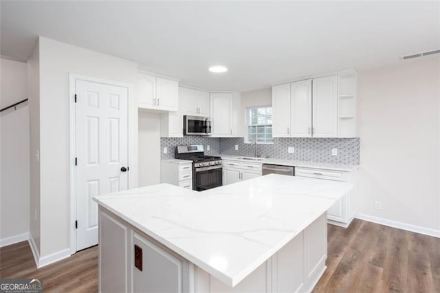 kitchen featuring light stone counters, stainless steel appliances, a kitchen island, white cabinetry, and sink