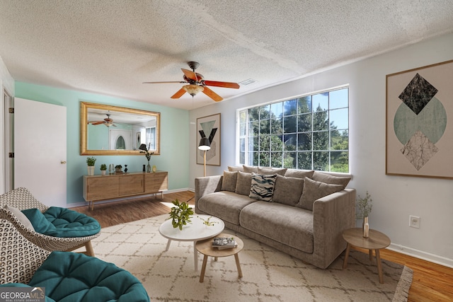 living area featuring wood finished floors, visible vents, a ceiling fan, baseboards, and a textured ceiling