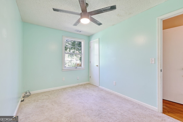 carpeted spare room with a textured ceiling, visible vents, baseboards, and ceiling fan